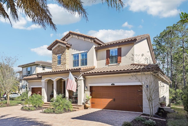 mediterranean / spanish-style home with stucco siding, an attached garage, and a tile roof