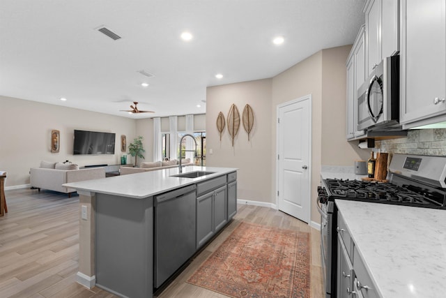 kitchen with sink, gray cabinetry, light hardwood / wood-style floors, stainless steel appliances, and a center island with sink