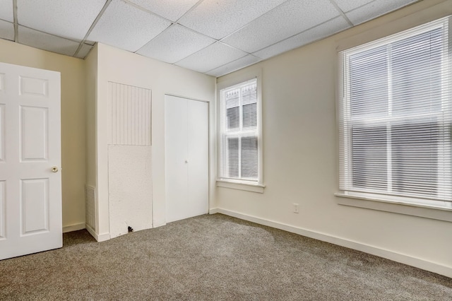 unfurnished bedroom featuring carpet floors, a drop ceiling, and a closet