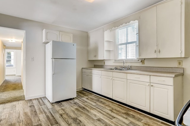 kitchen with white refrigerator, sink, white cabinets, and light hardwood / wood-style flooring