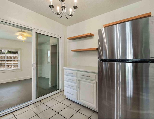 kitchen with white cabinets, hanging light fixtures, stainless steel fridge, light tile patterned floors, and a chandelier