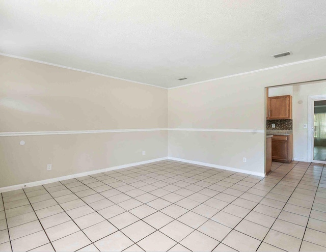 empty room with light tile patterned floors, a textured ceiling, and ornamental molding