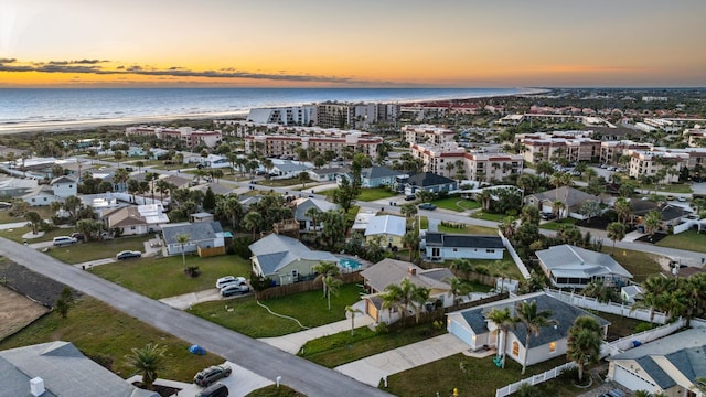 aerial view at dusk featuring a water view and a view of the beach