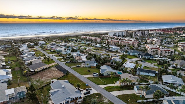 aerial view at dusk featuring a water view and a view of the beach