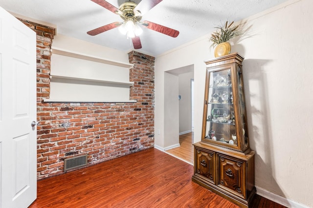 unfurnished living room with wood-type flooring, brick wall, a textured ceiling, and ceiling fan