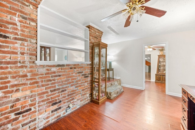 unfurnished living room with brick wall, a textured ceiling, and light hardwood / wood-style floors