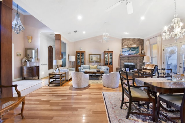 interior space featuring a brick fireplace, crown molding, light hardwood / wood-style floors, lofted ceiling, and ceiling fan with notable chandelier