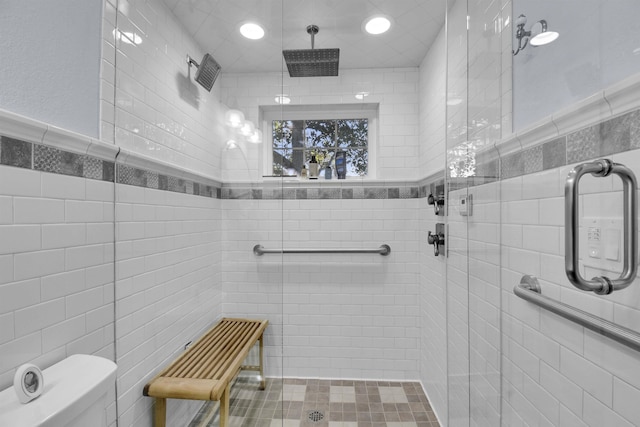 bathroom with toilet, an enclosed shower, and tile walls