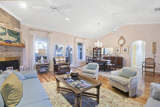 living room featuring lofted ceiling, ceiling fan with notable chandelier, crown molding, light wood-type flooring, and a fireplace