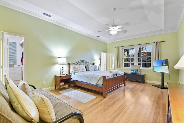 bedroom with ceiling fan, light wood-type flooring, crown molding, and a tray ceiling