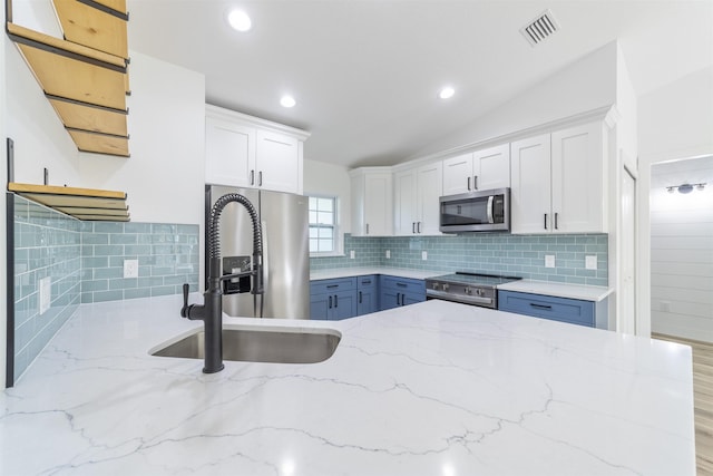 kitchen featuring visible vents, appliances with stainless steel finishes, white cabinets, vaulted ceiling, and a sink