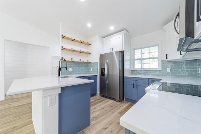 kitchen featuring stainless steel appliances, white cabinetry, a sink, light wood-type flooring, and a peninsula