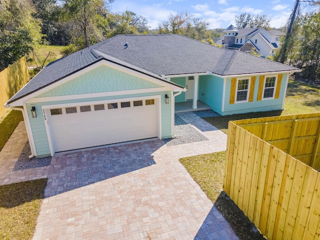 view of front of home featuring a garage, decorative driveway, roof with shingles, and fence