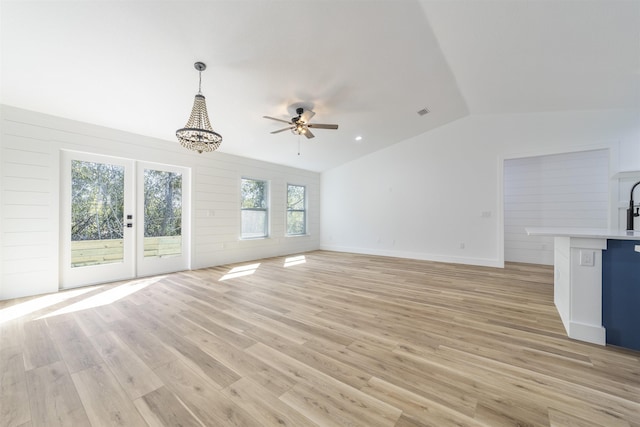 unfurnished living room with lofted ceiling, ceiling fan with notable chandelier, visible vents, light wood-style floors, and french doors