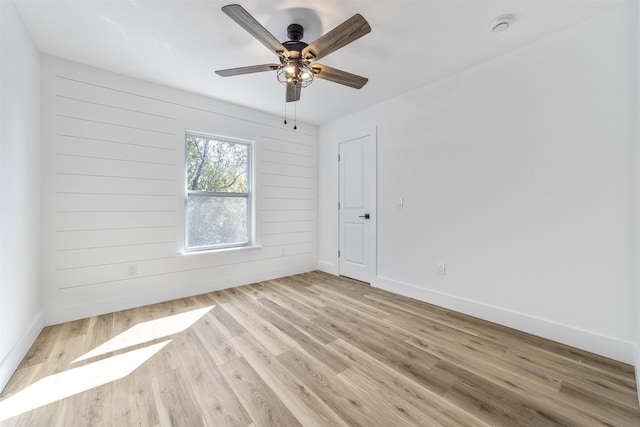 spare room featuring ceiling fan, wooden walls, light wood-style flooring, and baseboards