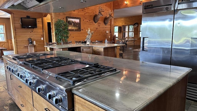 kitchen featuring appliances with stainless steel finishes, light brown cabinets, a kitchen island with sink, and wooden walls