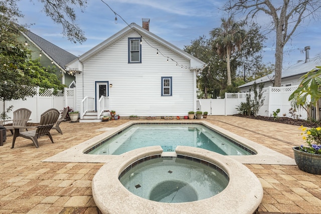 back of house with a patio area, a fenced backyard, a chimney, and a pool with connected hot tub