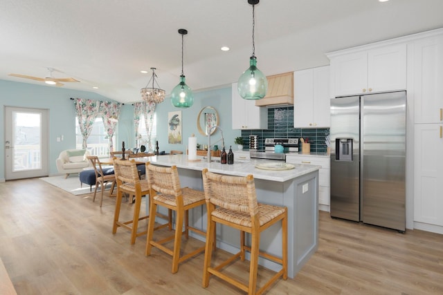 kitchen with a center island with sink, a kitchen breakfast bar, white cabinets, appliances with stainless steel finishes, and light hardwood / wood-style floors