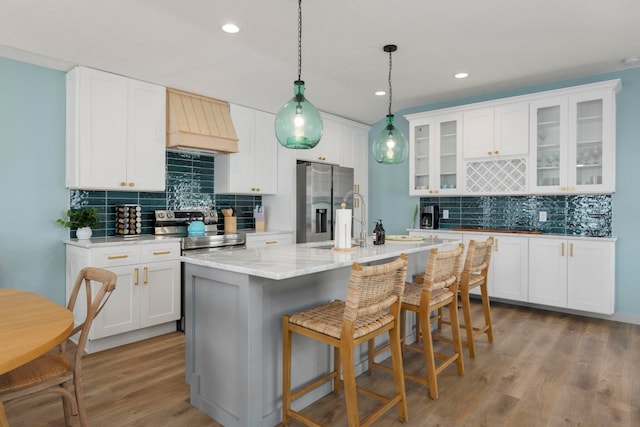 kitchen with custom exhaust hood, backsplash, white cabinets, appliances with stainless steel finishes, and light hardwood / wood-style floors