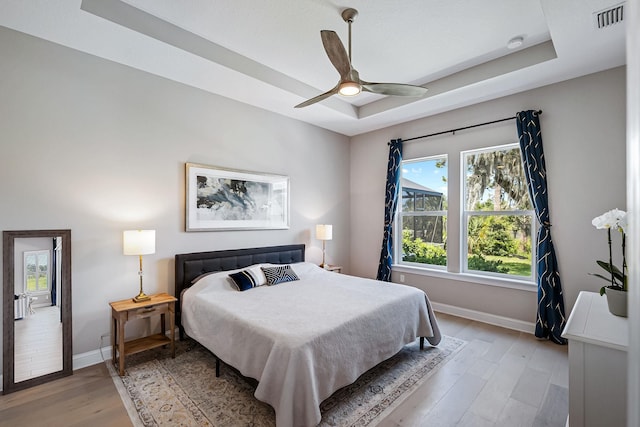 bedroom with a raised ceiling, ceiling fan, and light wood-type flooring