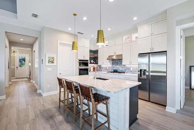 kitchen with sink, an island with sink, appliances with stainless steel finishes, decorative light fixtures, and white cabinetry