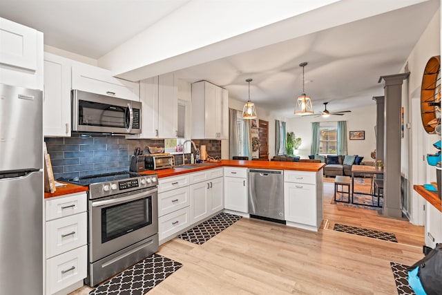 kitchen with tasteful backsplash, white cabinetry, kitchen peninsula, pendant lighting, and stainless steel appliances