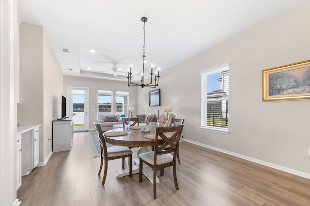 dining room featuring light wood-type flooring, a raised ceiling, and ceiling fan with notable chandelier