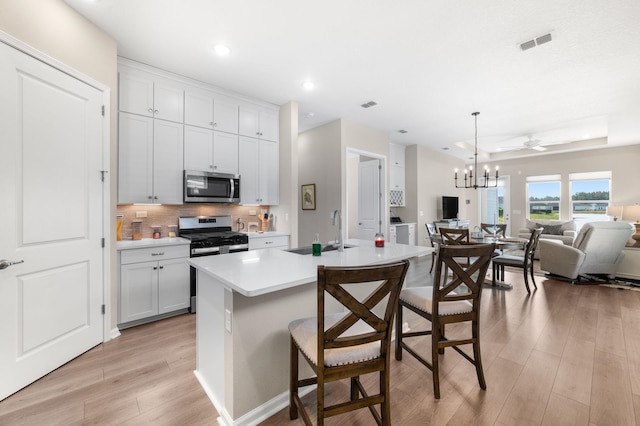 kitchen with a breakfast bar area, appliances with stainless steel finishes, an island with sink, pendant lighting, and sink