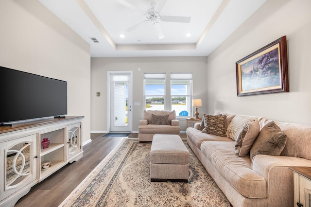 living room with dark wood-type flooring, a raised ceiling, and ceiling fan