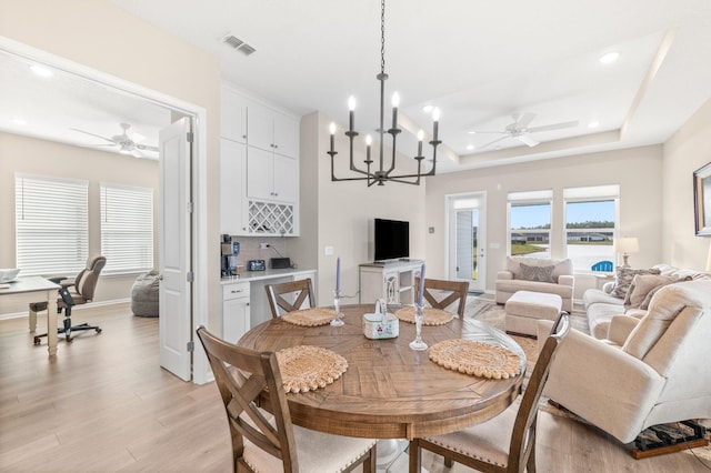 dining room with ceiling fan with notable chandelier, a tray ceiling, and light hardwood / wood-style flooring