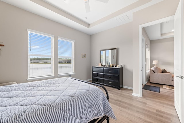 bedroom with ceiling fan, light wood-type flooring, and a raised ceiling