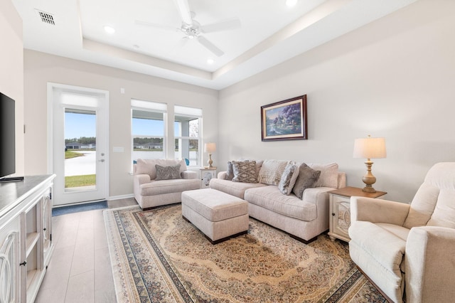 living room featuring ceiling fan, light wood-type flooring, and a tray ceiling