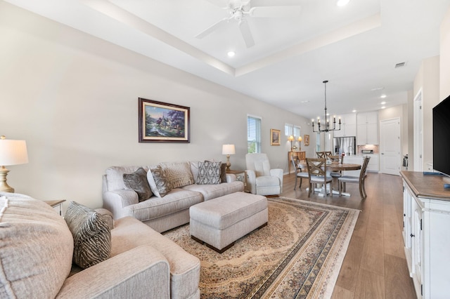 living room with ceiling fan with notable chandelier, light hardwood / wood-style floors, and a tray ceiling