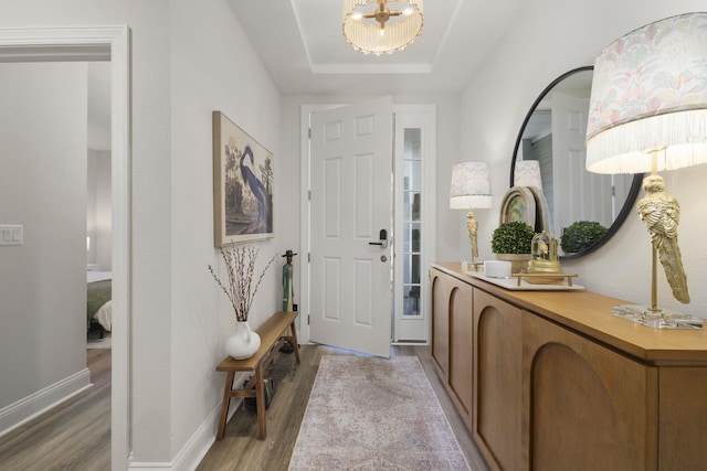 foyer with light wood-type flooring, a chandelier, baseboards, and a raised ceiling