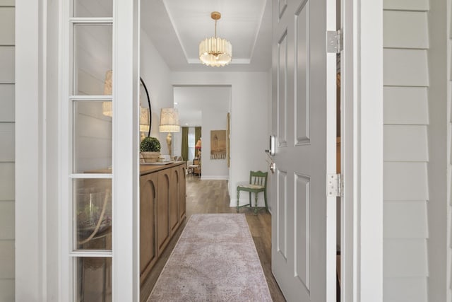 hall featuring dark wood-type flooring, a raised ceiling, baseboards, and a chandelier