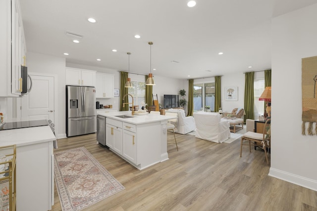 kitchen with appliances with stainless steel finishes, a sink, open floor plan, white cabinets, and recessed lighting