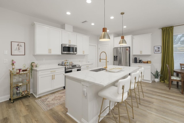 kitchen with appliances with stainless steel finishes, a sink, light wood-type flooring, a kitchen island with sink, and recessed lighting