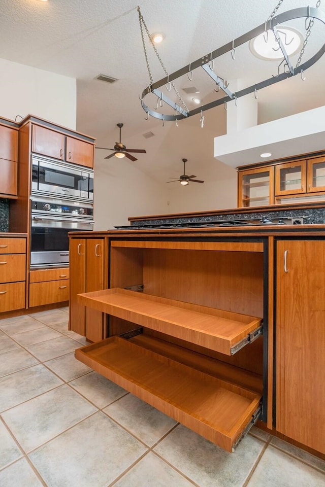 kitchen featuring visible vents, dark countertops, stainless steel microwave, brown cabinets, and a textured ceiling