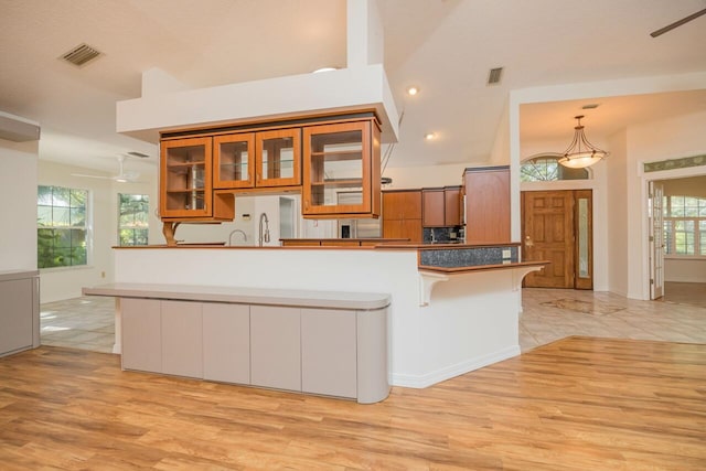 kitchen featuring a peninsula, visible vents, brown cabinetry, and glass insert cabinets