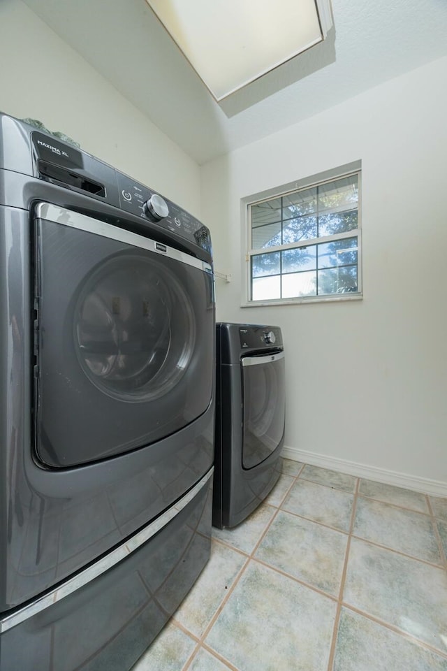 laundry room featuring light tile patterned floors, laundry area, washing machine and dryer, and baseboards