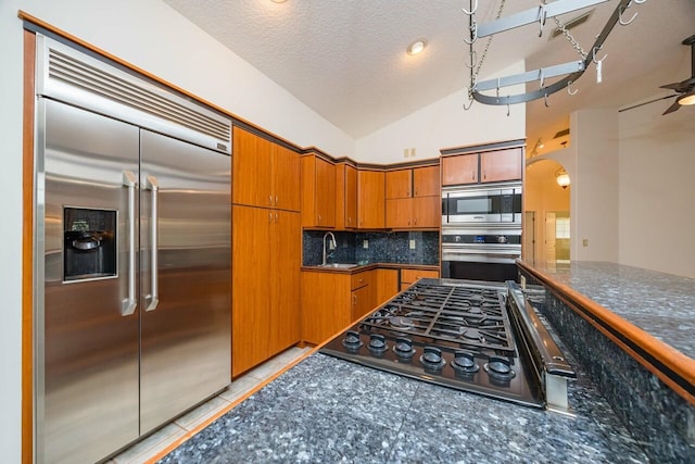 kitchen with built in appliances, dark countertops, and a sink