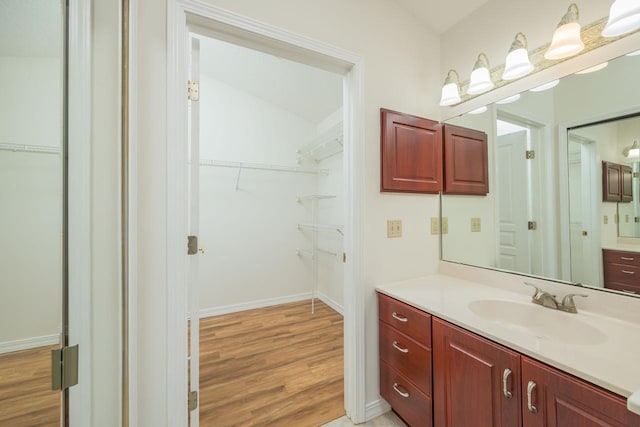 full bathroom with a spacious closet, wood finished floors, vanity, and baseboards