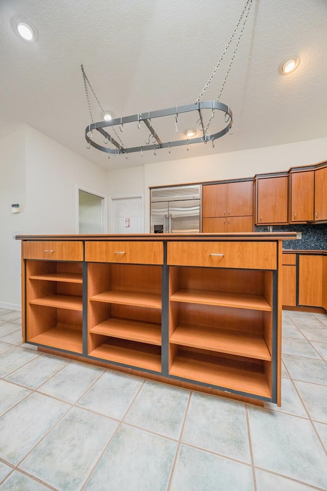 interior space with light tile patterned floors, brown cabinets, stainless steel built in refrigerator, a textured ceiling, and open shelves