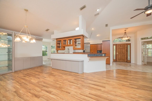 kitchen with brown cabinets, a wealth of natural light, visible vents, glass insert cabinets, and fridge