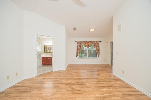 spare room featuring light wood-type flooring, baseboards, visible vents, and vaulted ceiling