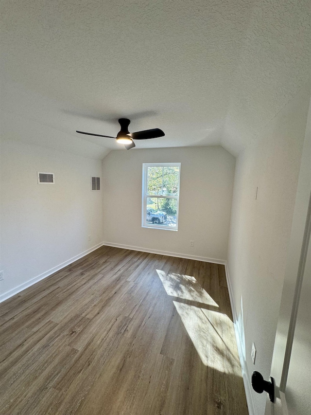 spare room with vaulted ceiling, visible vents, a textured ceiling, and dark wood-style flooring