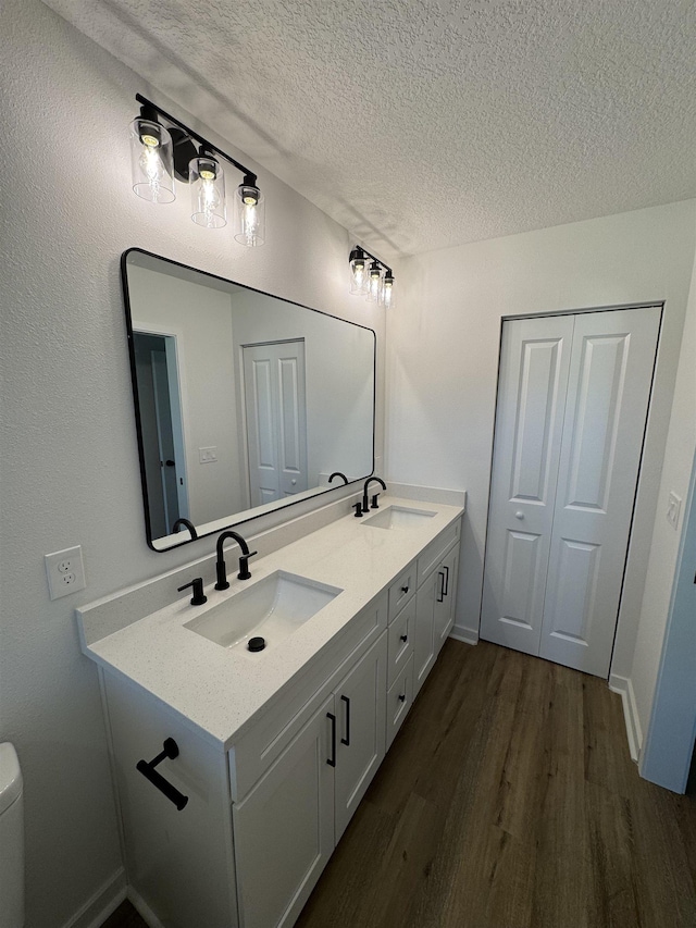 bathroom featuring a sink, a textured ceiling, wood finished floors, and double vanity