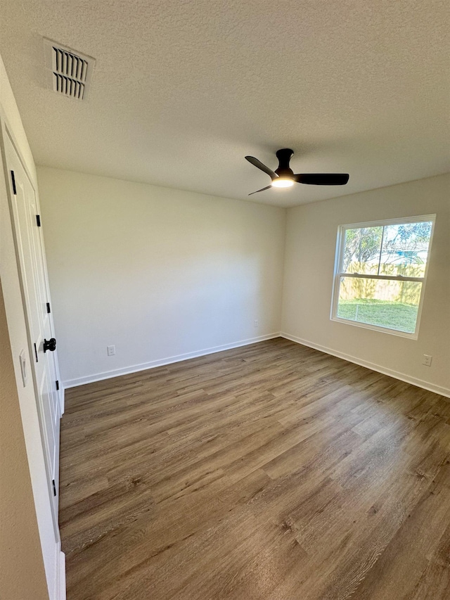 spare room featuring visible vents, a textured ceiling, dark wood-style flooring, and a ceiling fan