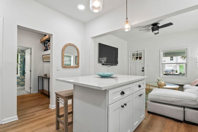 kitchen featuring light wood-type flooring, white cabinets, a kitchen island, decorative light fixtures, and open floor plan