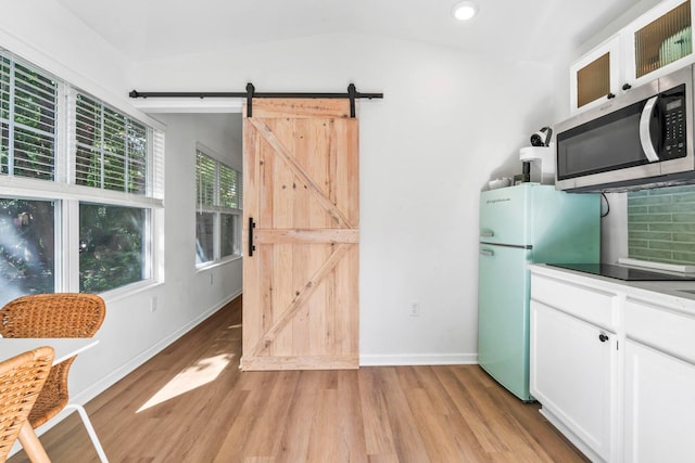 kitchen with stainless steel microwave, a barn door, light wood-style flooring, and white cabinets